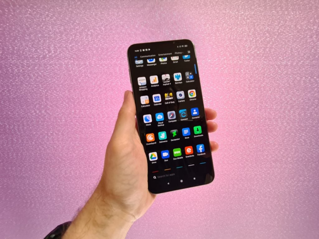 A black smartphone held in hand on a pink-purple background