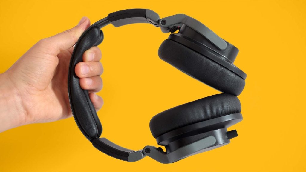 Gray-black Hi-X55 headphones held in hand on a solid-yellow background