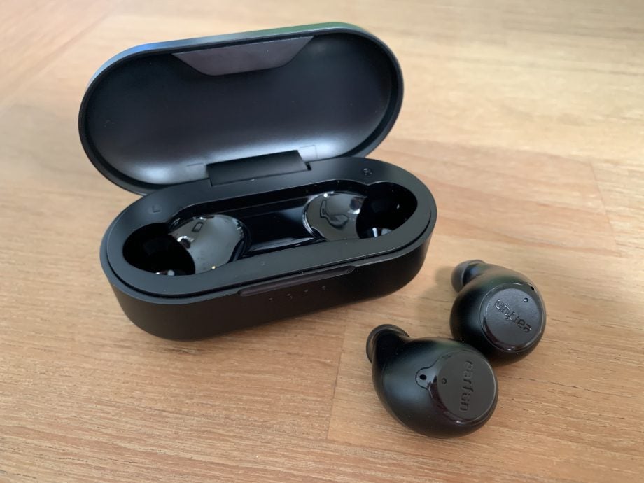 Black Earfun Free earbuds resting on a table with it's case standing behind
