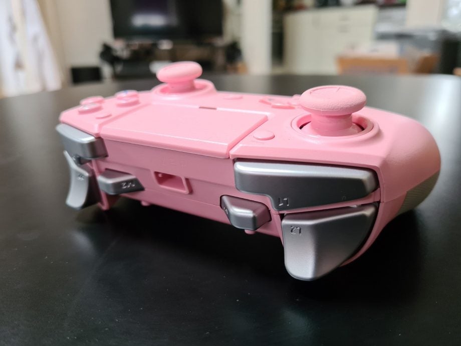 Top back side view of a pink Razer Raiju tournamet gaming controller resting on a black table