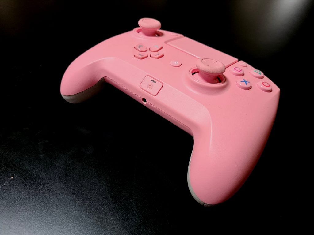 A pink Razer Raiju tournamet gaming controller resting on a black table