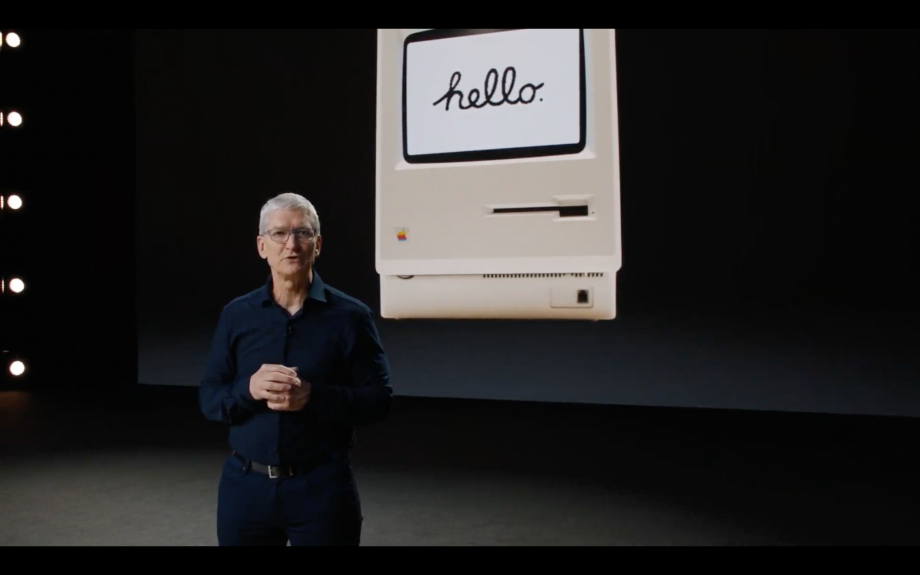 Tim Cook standing on a black stage with hello in a machine displayed on screen behind him