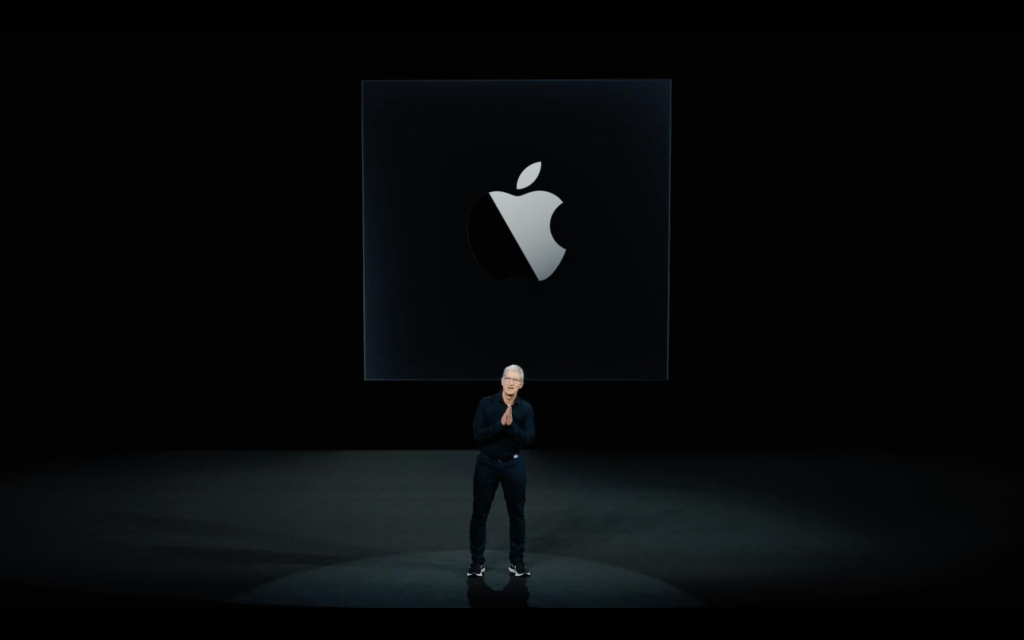 Tim Cook standing on a stage with Apple logo displayed on a screen behind him