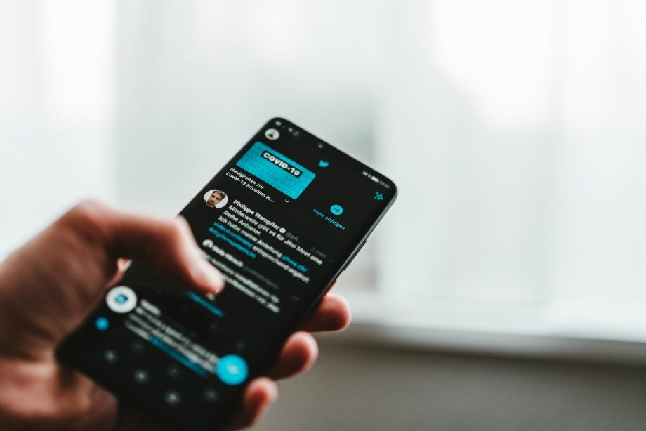 A black smartphone held in hand displaying tweets on Twitter