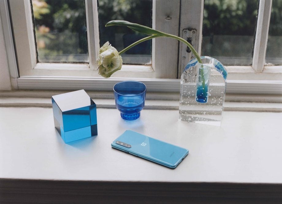 A blue One Plus smartphone laid upside down on a white platform beside a window
