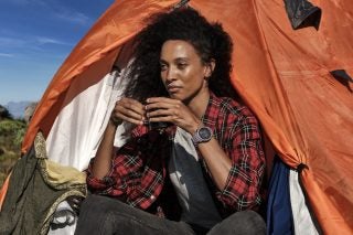 A women sitting against a tent wearing a purple Fenix 6 Solar watch