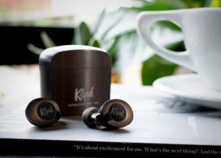 Brown Klipsch T5 II earbuds resting on a table with it's case resting behind