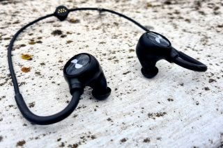 Black Nuraloops wireless earphones resting on a concrete floor
