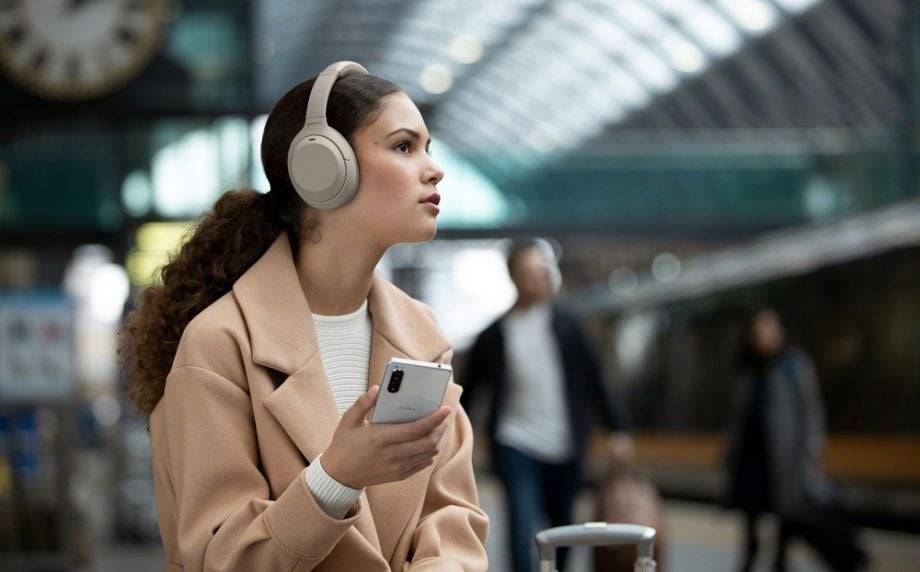 A girl holding a white smartphone wearing Sony WH1000 XM4 headphones