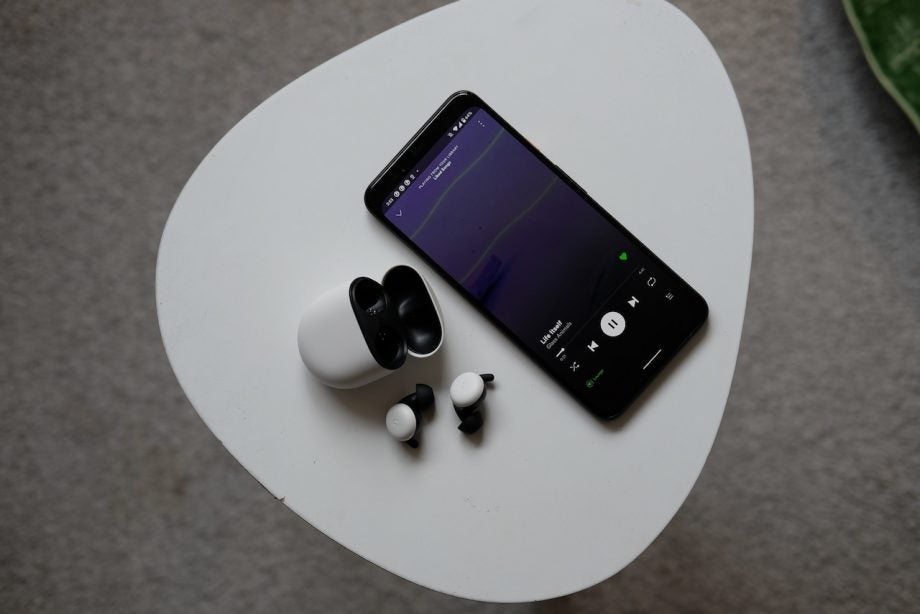 View from top of a smartphone playing music and Pixel Buds resting beside