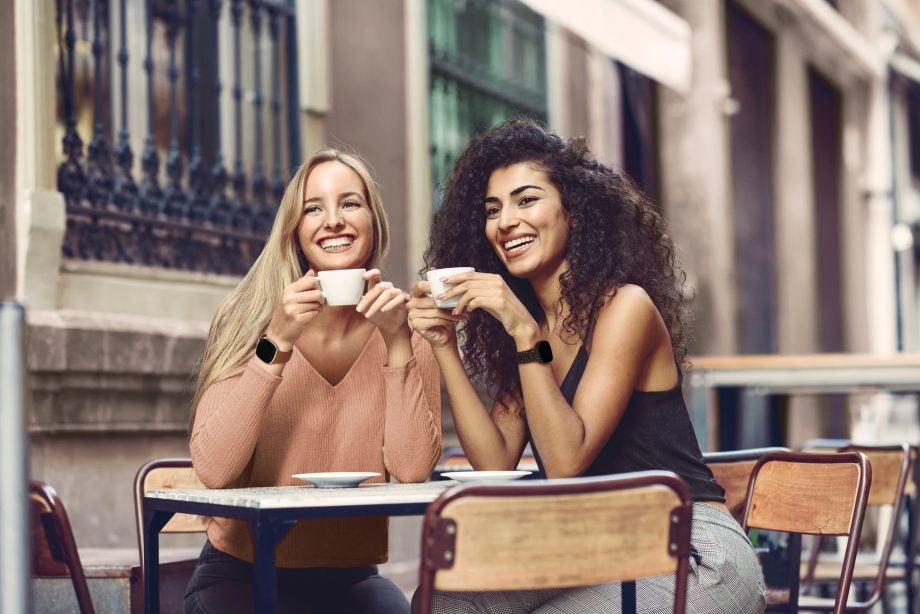 Two women sitting and drinking coffee wearing Fitbit Versa 3