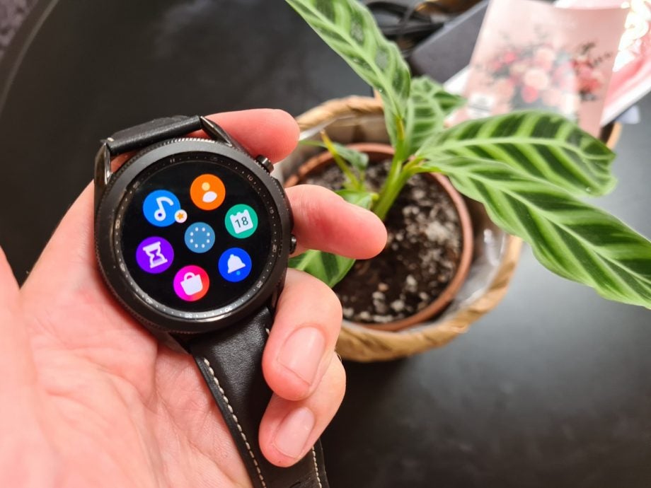 A black Galaxy watch 3 held in hand displaying apps