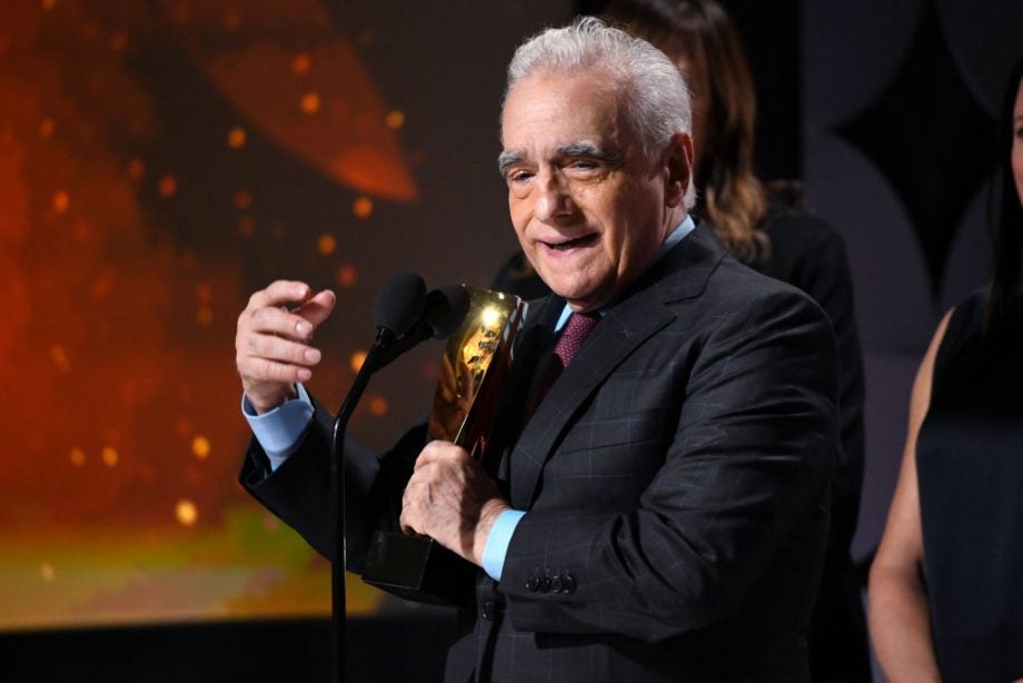 An old man in black outfit holding an award standing behind a mic