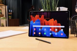 A black Samsung Galaxy Tab S7 plus standing on a table displaying home screen