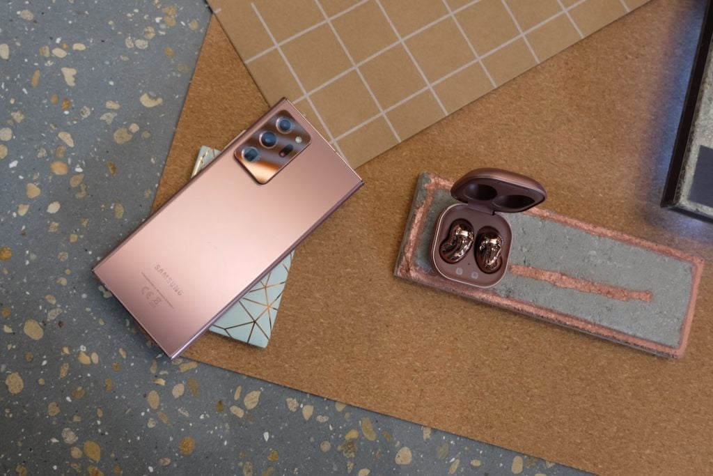 View from top of a brownish-pink Samsung Galaxy Note 20 Ultra laid upside down on a table with Galaxy Buds live beside