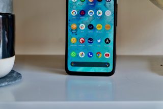 Close up image of a black Google Pixel 4a standing on a white shelf displaying homescreen