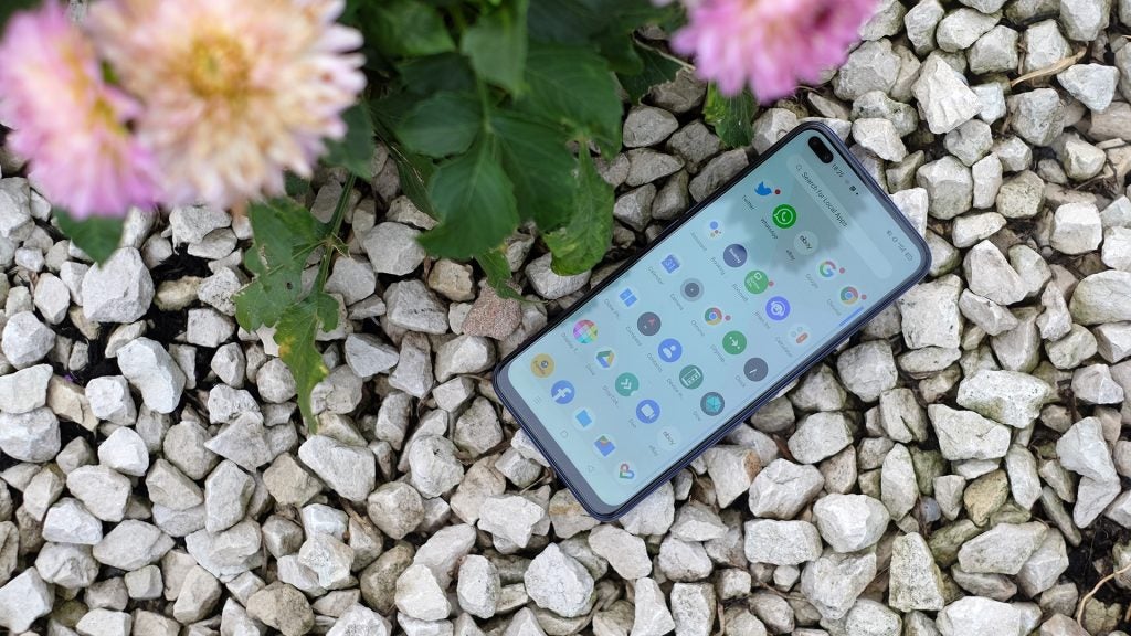 A Realme X50 smartphone laid on pebbles displaying menu screen