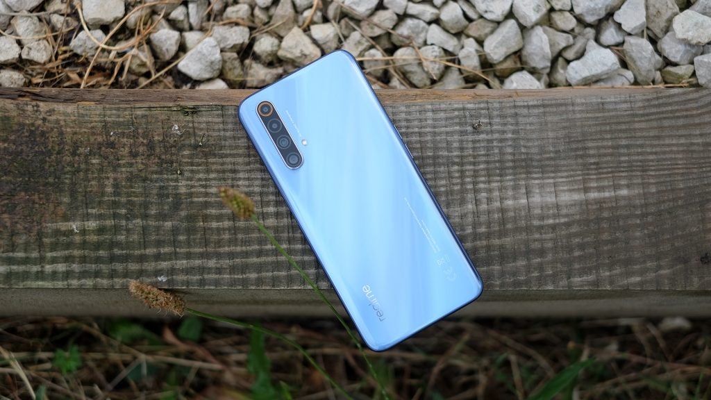 A Realme X50 smartphone laid upside down on a wooden plank, back panel view