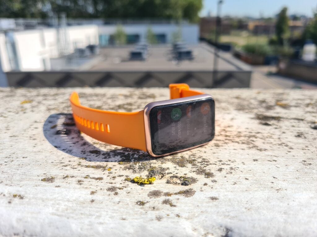 An orange-black Huawei watch fit laying on a concrete floor