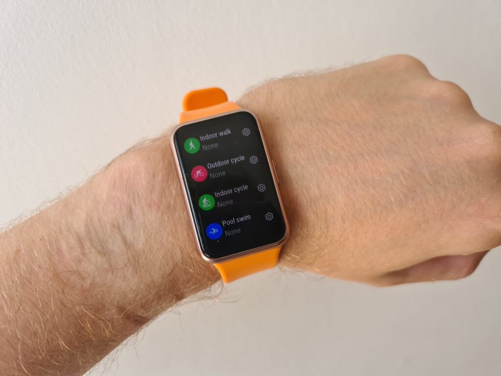 An orange-black Huawei watch fit tied to a wrist displaying workouts
