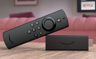 A black Fire TV stick lite laid on a wooden table with it's remote leaning on it