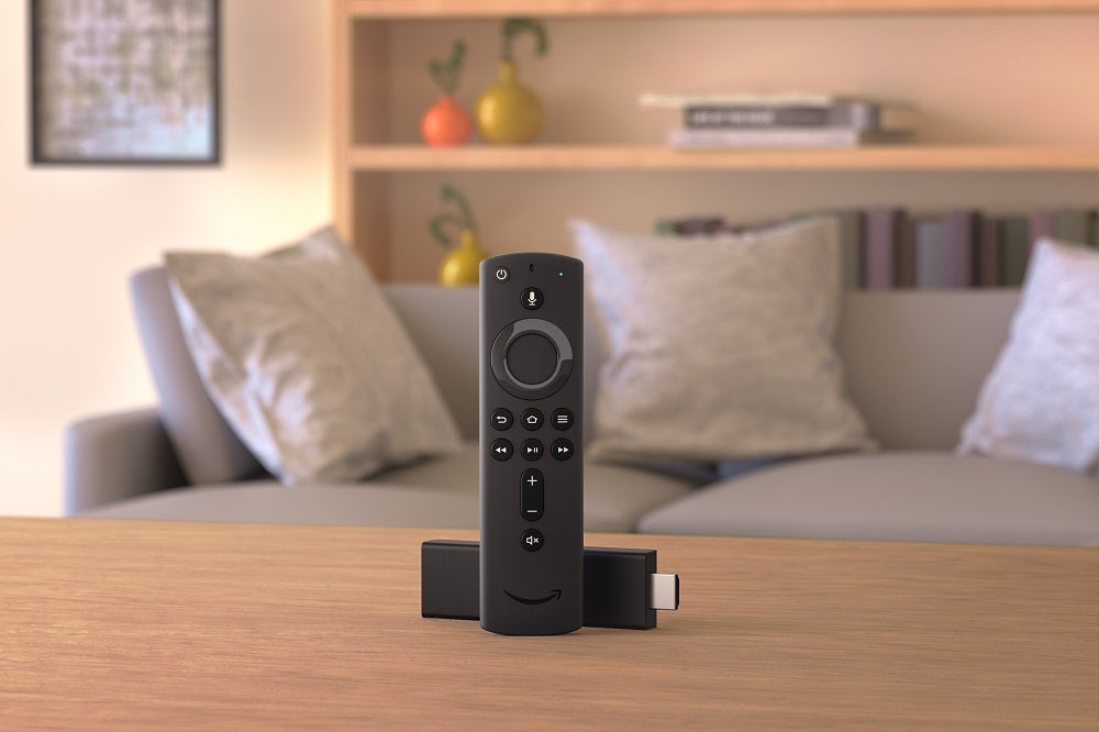 A black Fire TV stick laid on a wooden table with it's remote standing in front of it