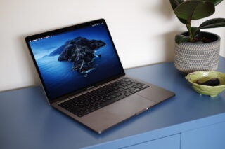 Left angled view of a silver Macbook Pro standing on a blue table displaying homescreen