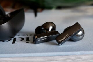 Black Huawei earbuds earbuds resting on a book with it's case resting beside