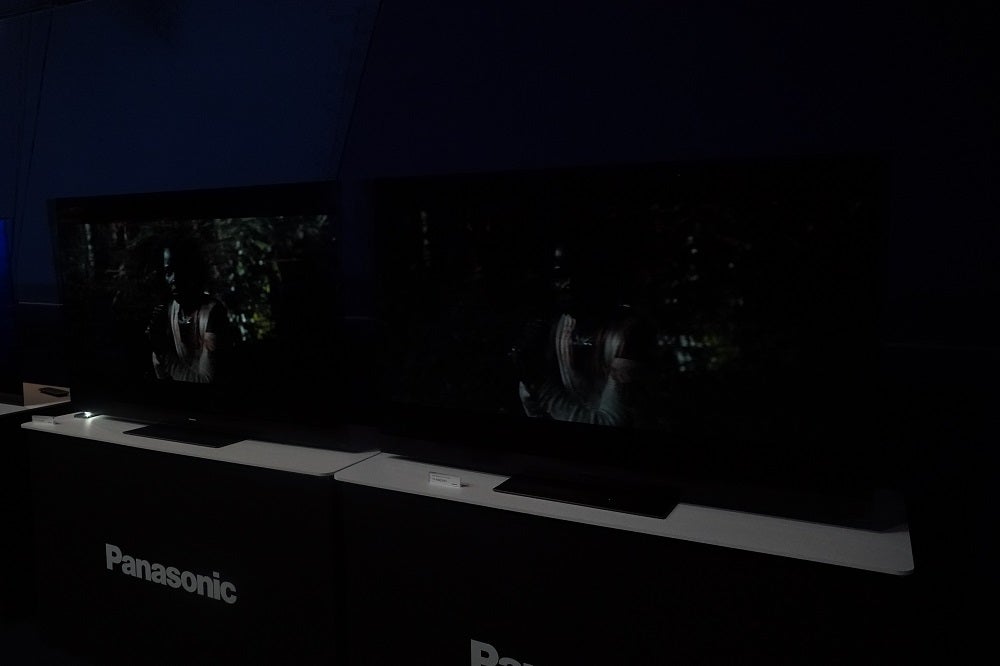 Two black Panasonic TVs standing on tables in dark displaying scene in Dolby Vision IQ