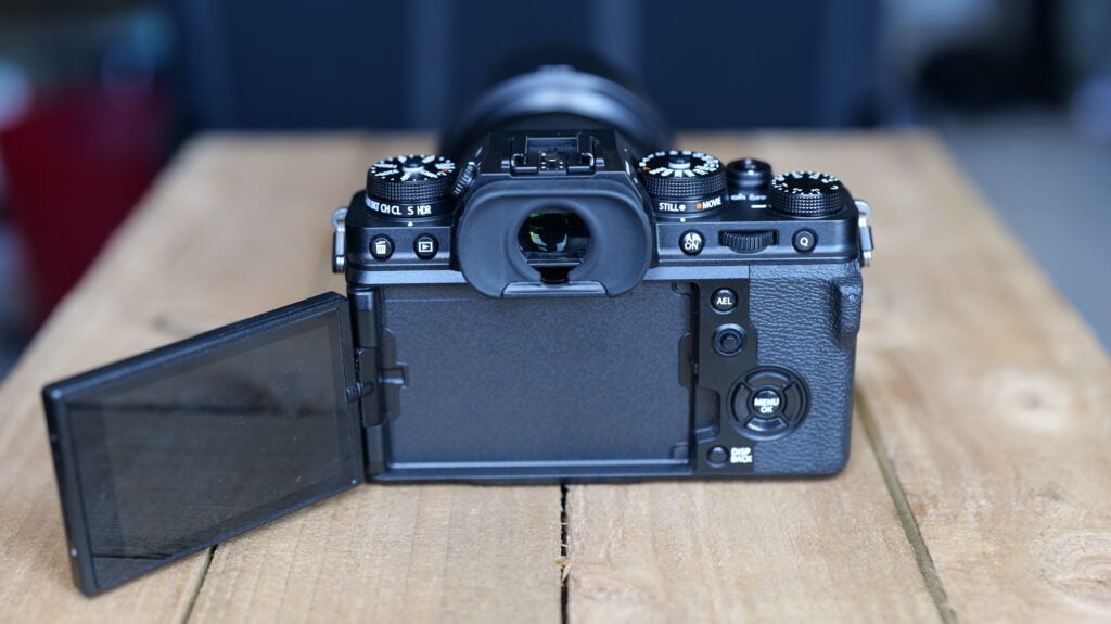 Back side view of a black Fujifilm XT4 camera standing on a wooden table with it's screen flipped open