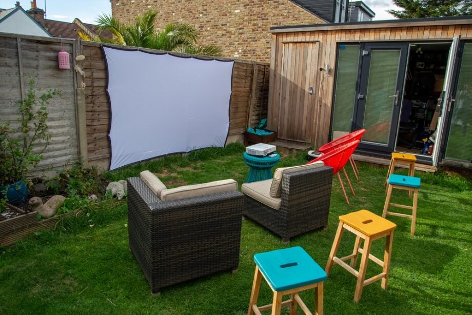 A cinema set up in a garden with projection screen, projector, and chairs all around