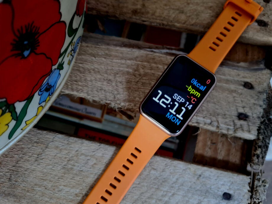 An orange-black Huawei watch fit laid on wooden planks