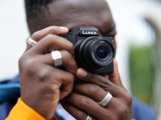 A man helding a black Lumix G100 camera near his eye to click photos