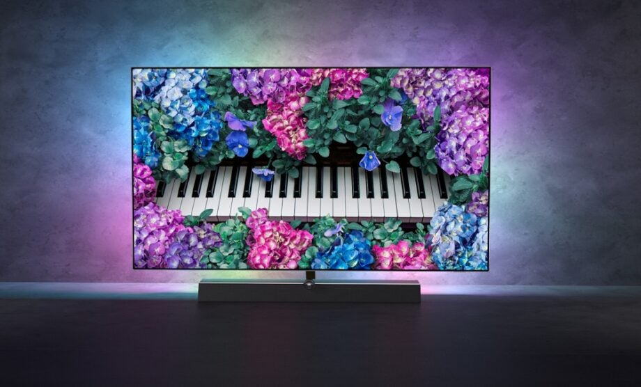 A Philips OLED 935 TV standing on dark background displaying a colorful wallpaper
