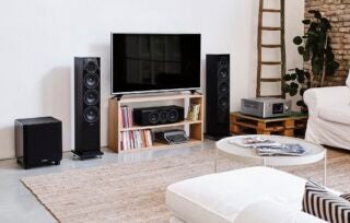 Black Sonus Lumina 5.1 speakers standing on sides of a TV in a living room