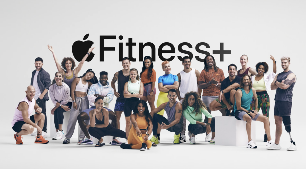 A number of people standing in workout clothes in front of Apple Fitness + logo on a white wall