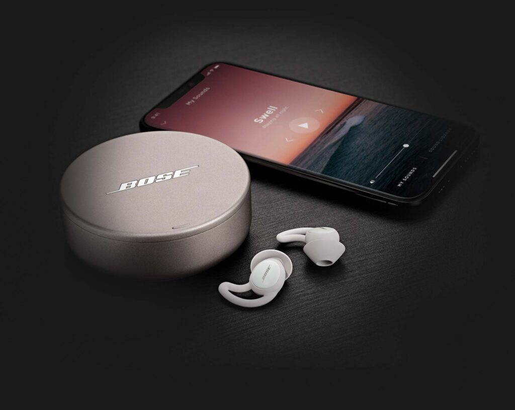White Bose earbuds resting with it's case behind and a smartphone laid beside