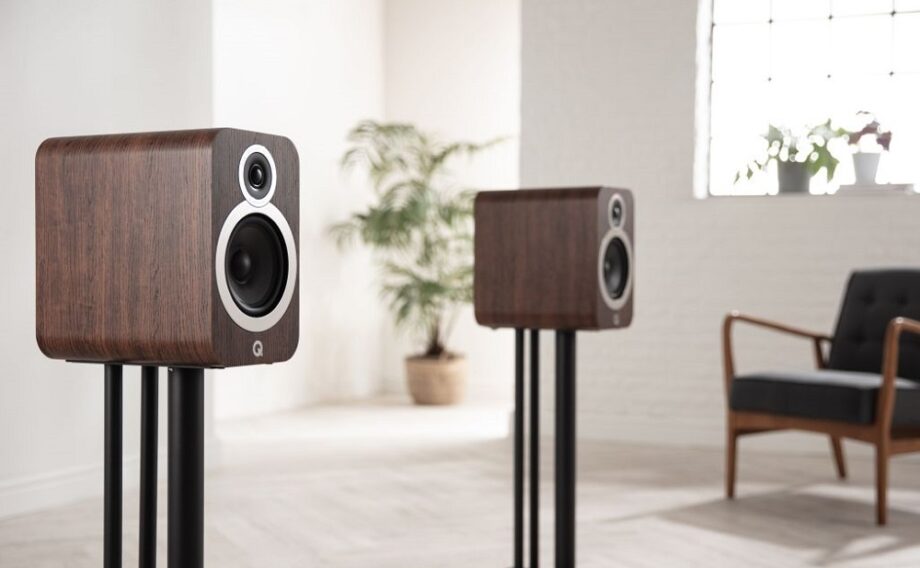 Two wooden finish Qacoustics 3030i speaker standing on a stand in a living room