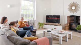 A family sitting on a couch looking at a TV displaying Freeview Play TV guide