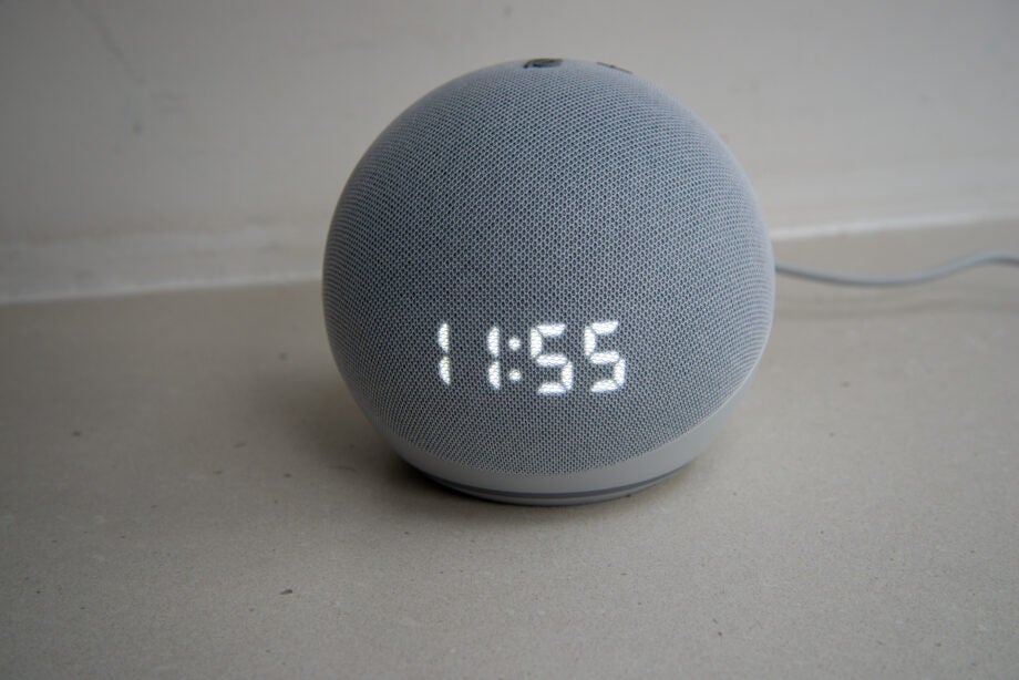 A silver round Amazon Echo 4th gen speaker standing on floor displaying time on itself