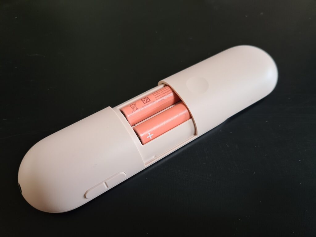A pink Chromcast's remote laid upside down on a table with open batteries panel