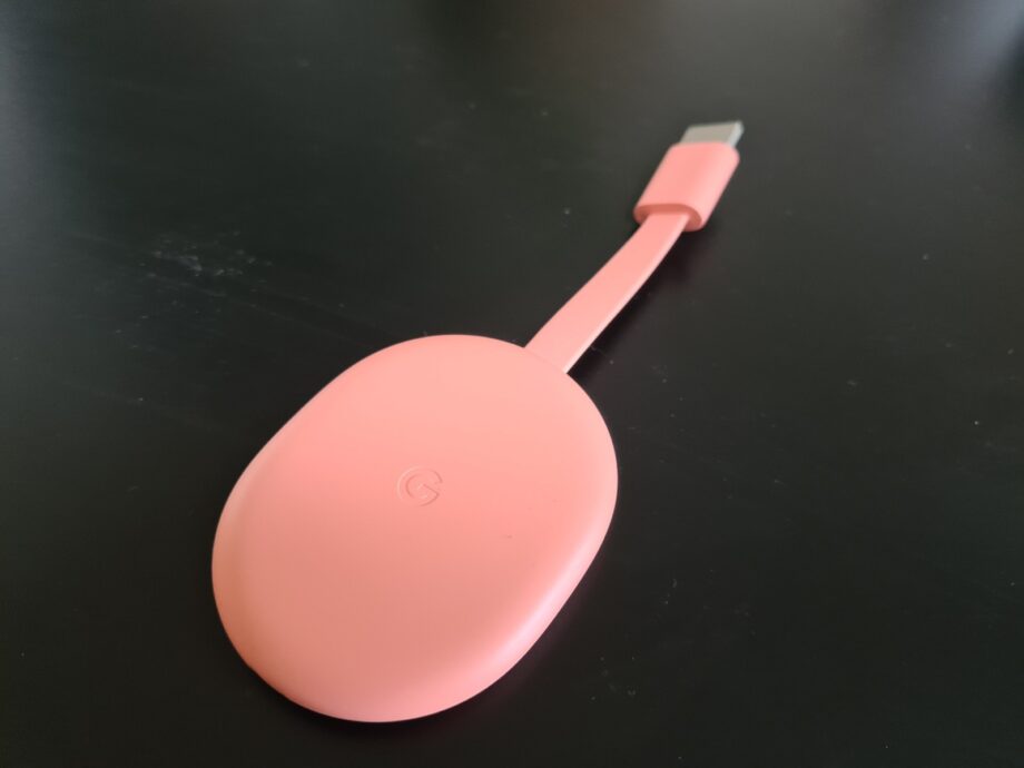 A pink Chromecast resting on a black table