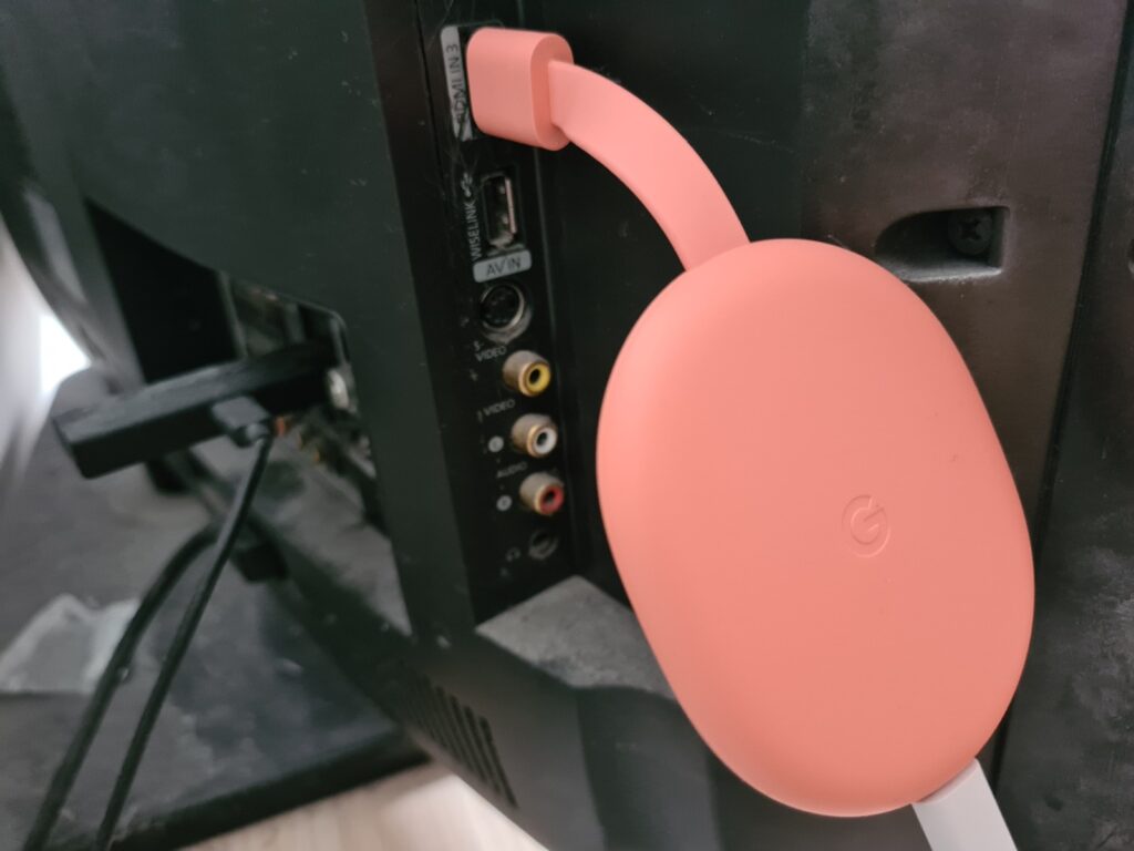 Chromecast with Google TVA pink Chromecast plugged into a TV's ports section on the back