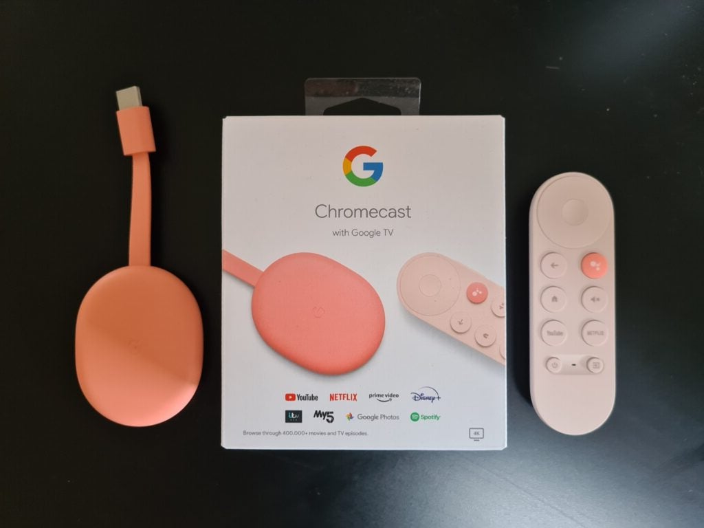 Chromecast with Google TVA pink Chromecast with it's remote and packaging box resting on a black table, view from top