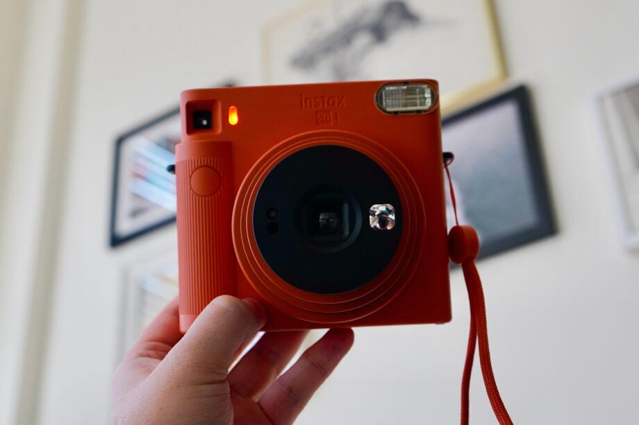 A orange-black InstaX camera held in hand