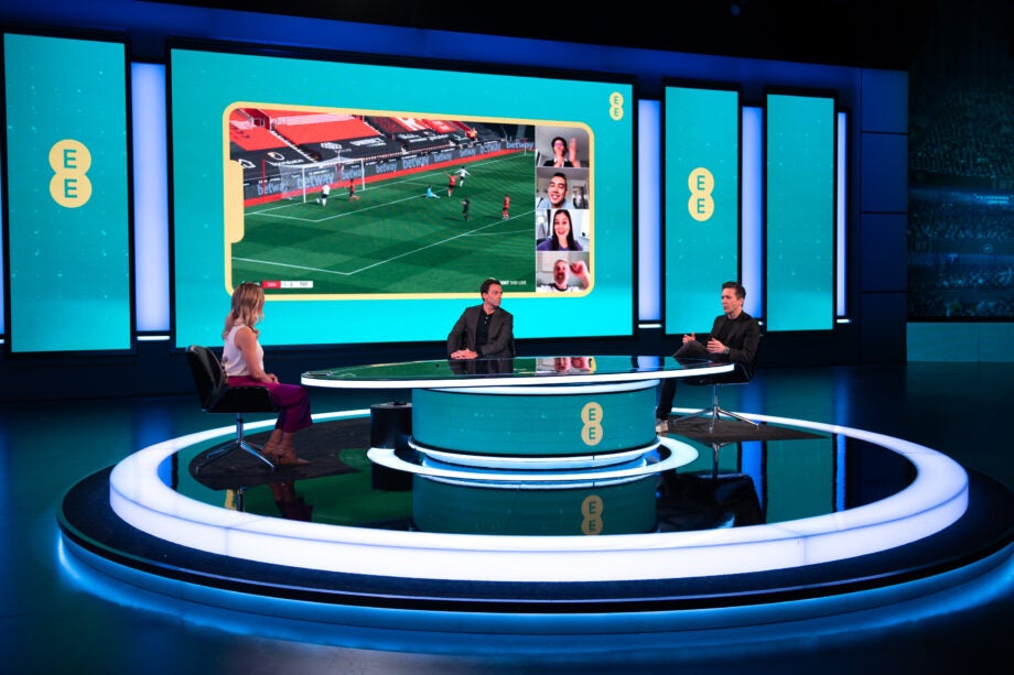 Three people sitting around a round table with BT sport displayed on a phone on the screen behind