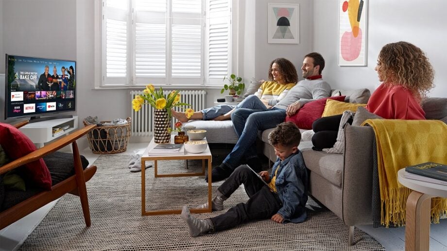 A family sitting on a couch looking at a TV displaying content to stream on Android TV's homescreen