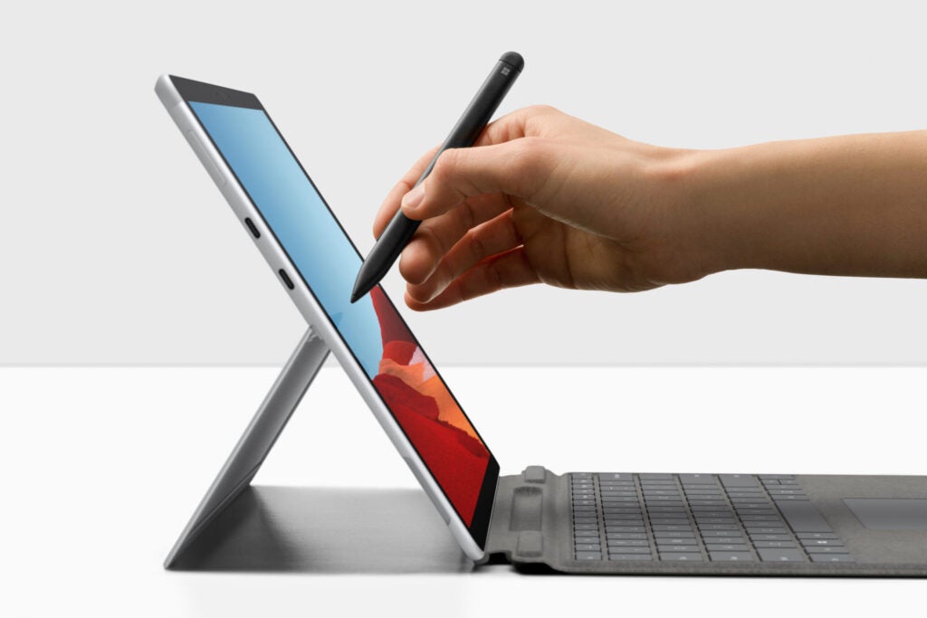 Left side edge view of a silver Surface pro X standing on a white table