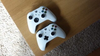 Two white Xbox controllers on a wooden table, view from top