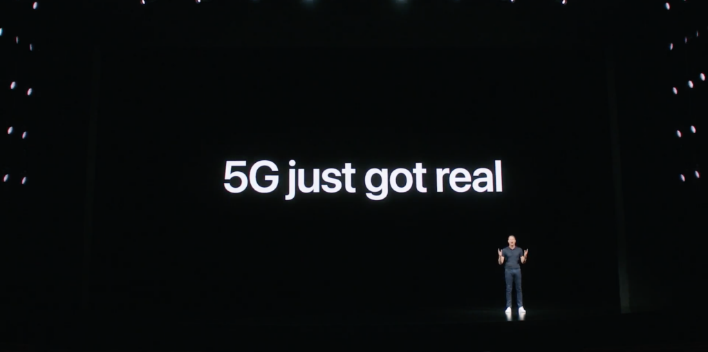 A guy standing on a black stage with 5G just got real displayed on a screen behind